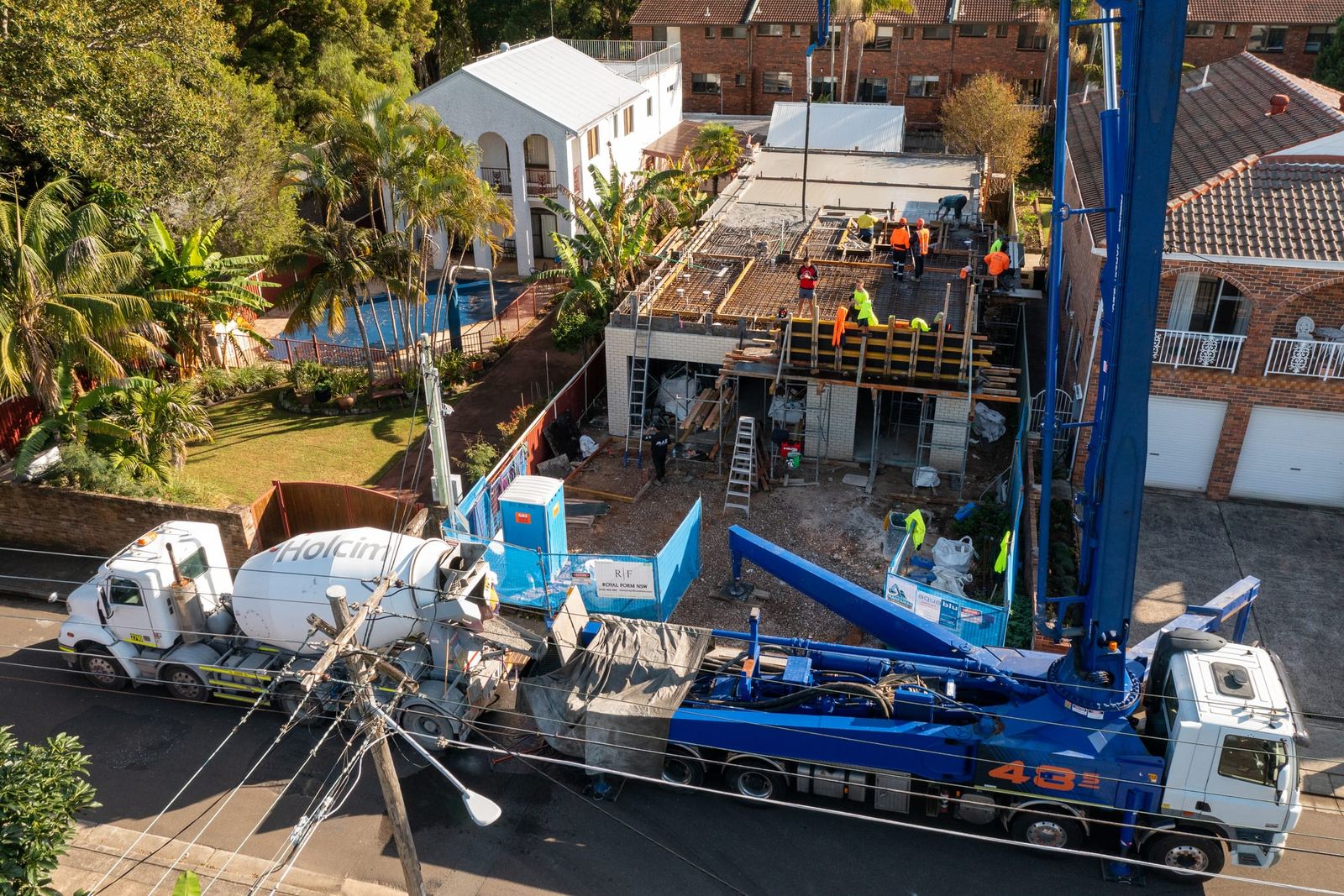 Boom pump and agitator truck parked on the street, the boom extended over the new first-floor slab