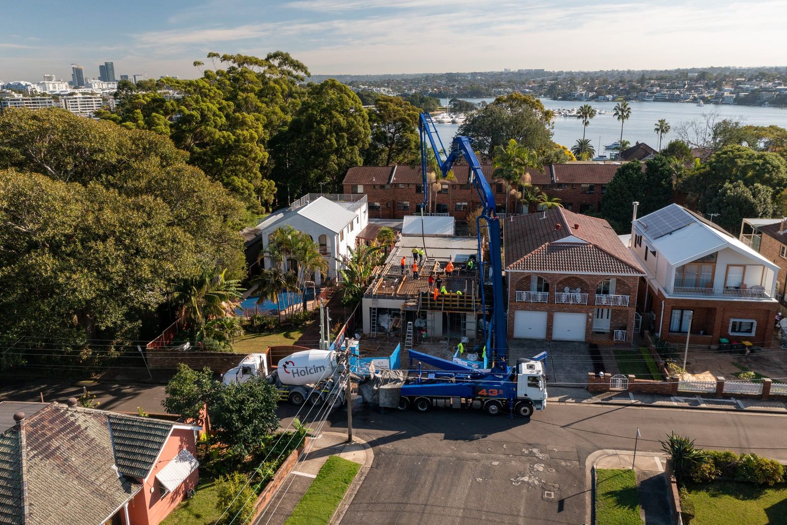 The home under construction between neighbouring houses, pump boom raised over the deck and the river beyond