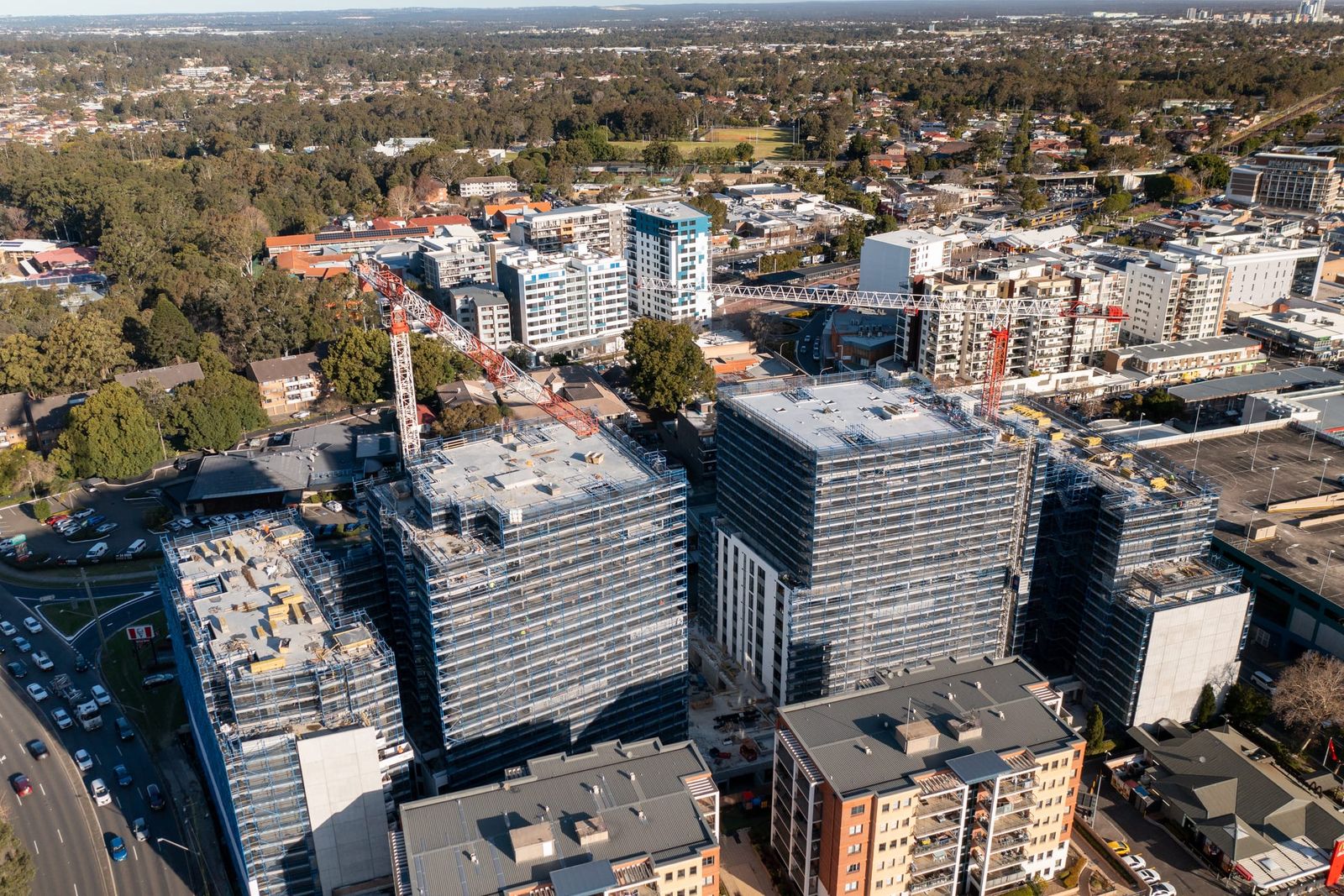 Close aerial of the scaffold wrap on the towers, a tower crane between them and traffic on the road below