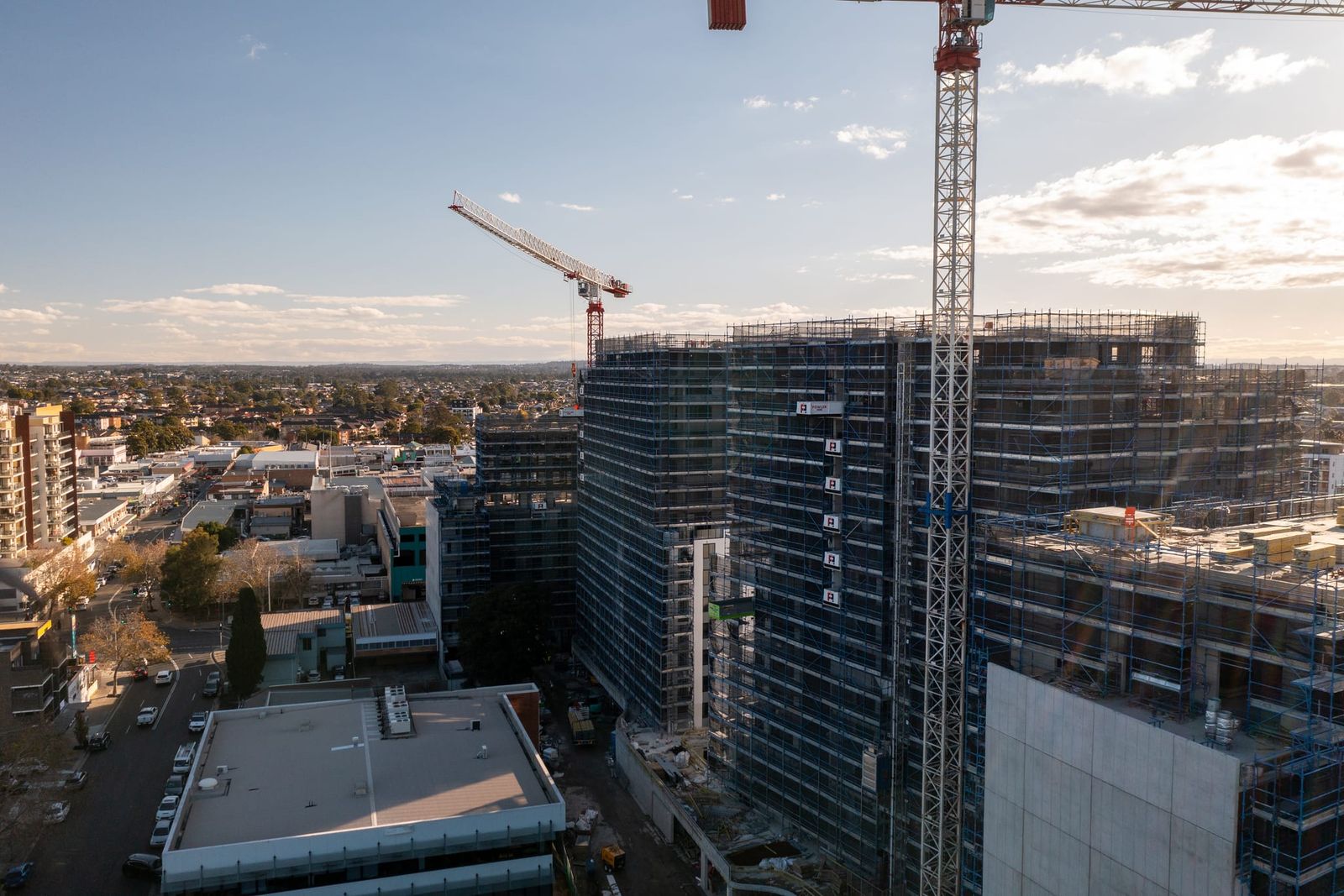 Low view of a scaffolded tower face, tower cranes against the afternoon sky