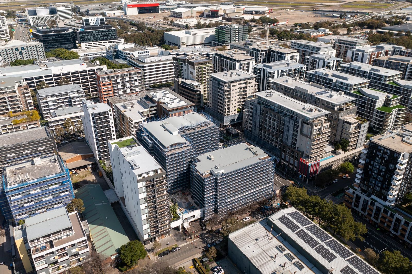 High view across the Mascot precinct, the scaffolded pair among apartment blocks and rooftop solar