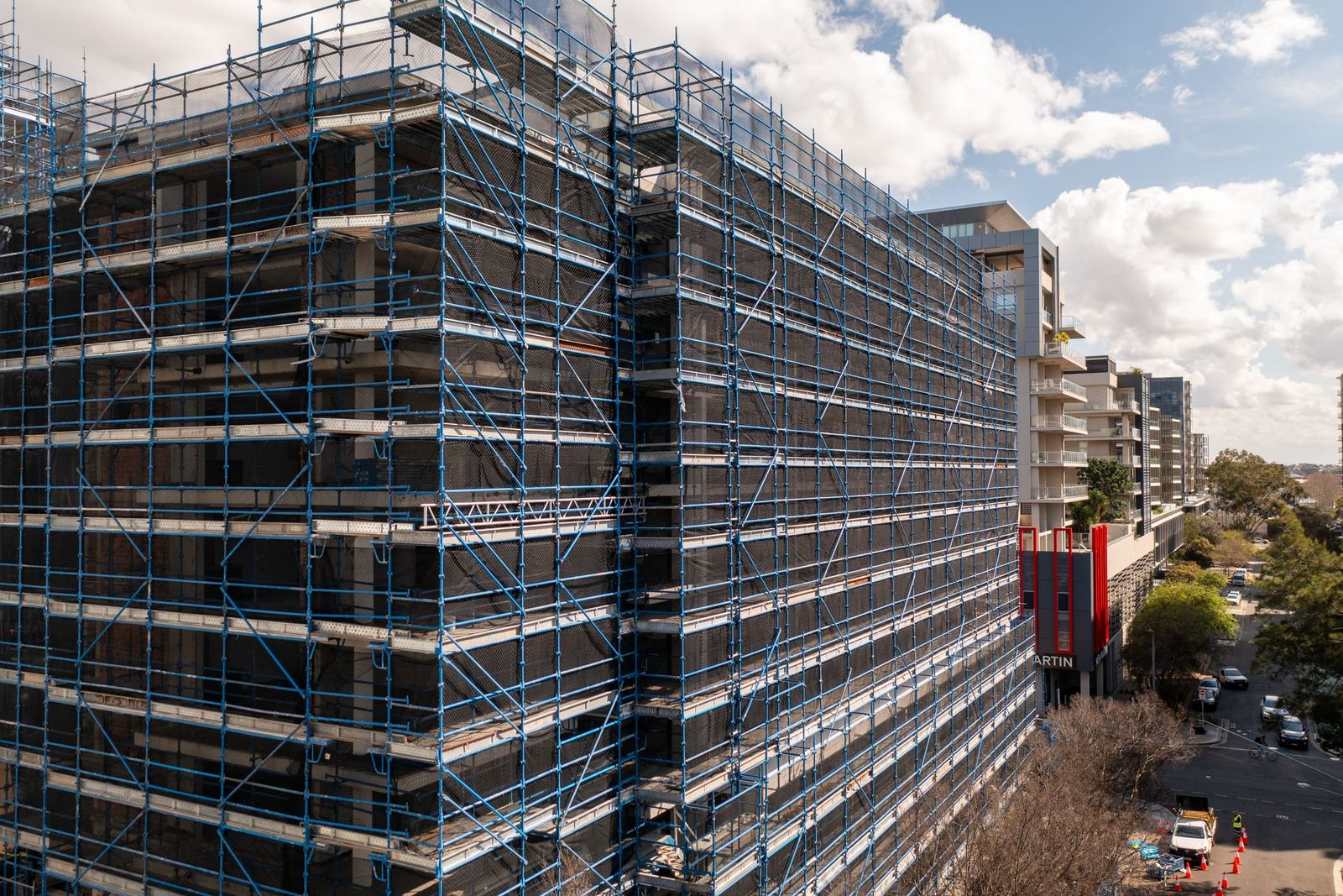 Low view of the scaffold across two faces of a building, the street and trees below