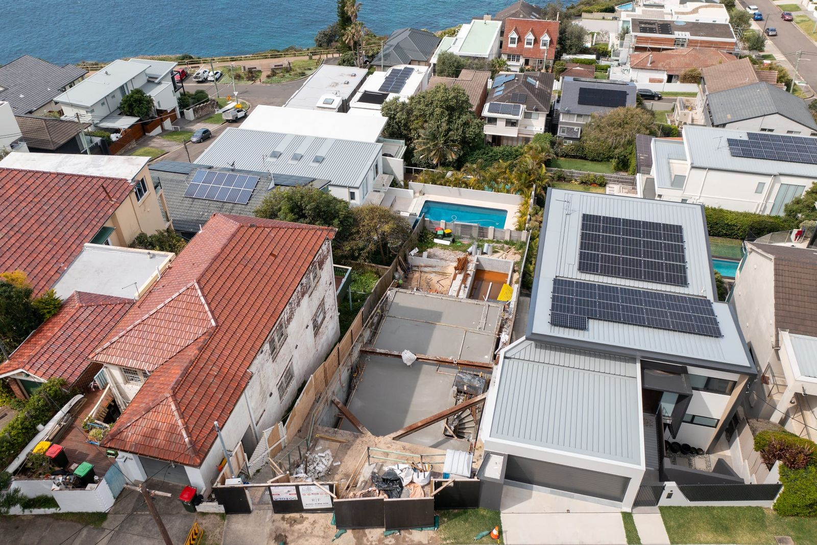 The narrow site between a tiled-roof house and a modern home with rooftop solar, the ocean at the top of frame