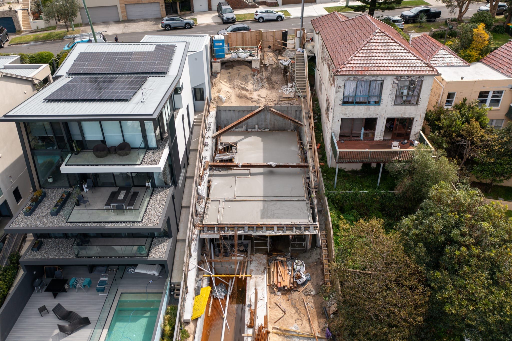 Looking down the length of the block at formwork and props for the new slab, beside a glass-fronted home with a pool