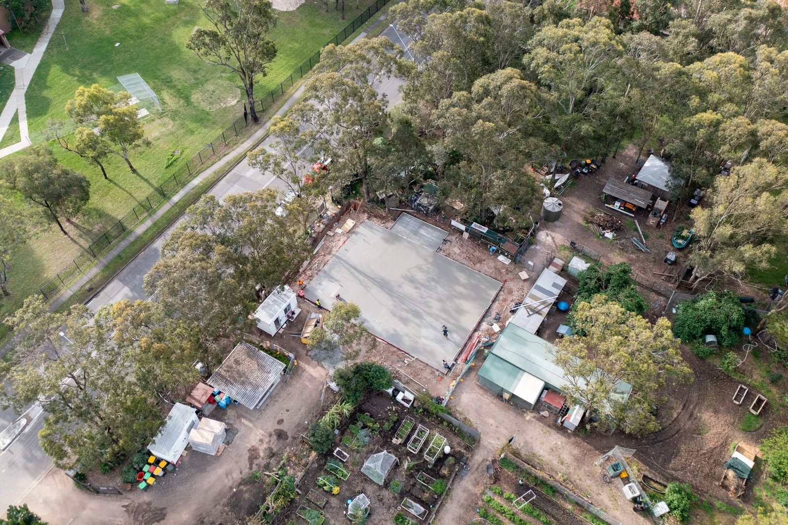 High view of the slab beside a park and a tree-lined road, garden plots and sheds on the neighbouring land