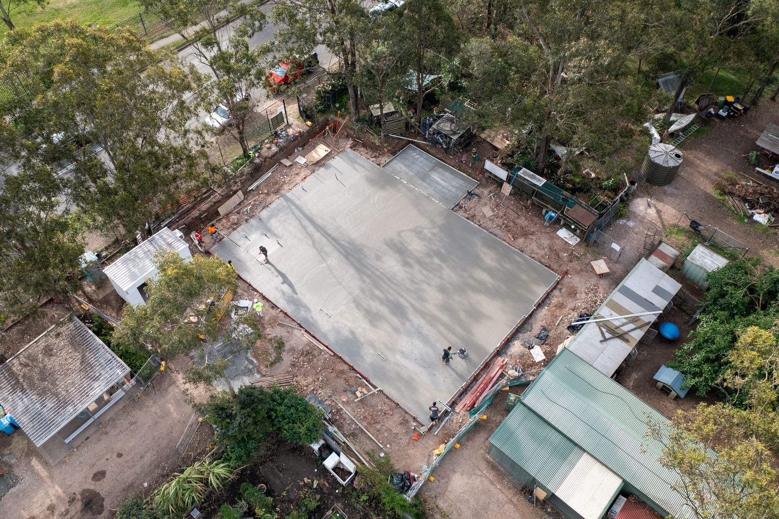 The ground slab from an angle, workers finishing the concrete with sheds and trees around the site