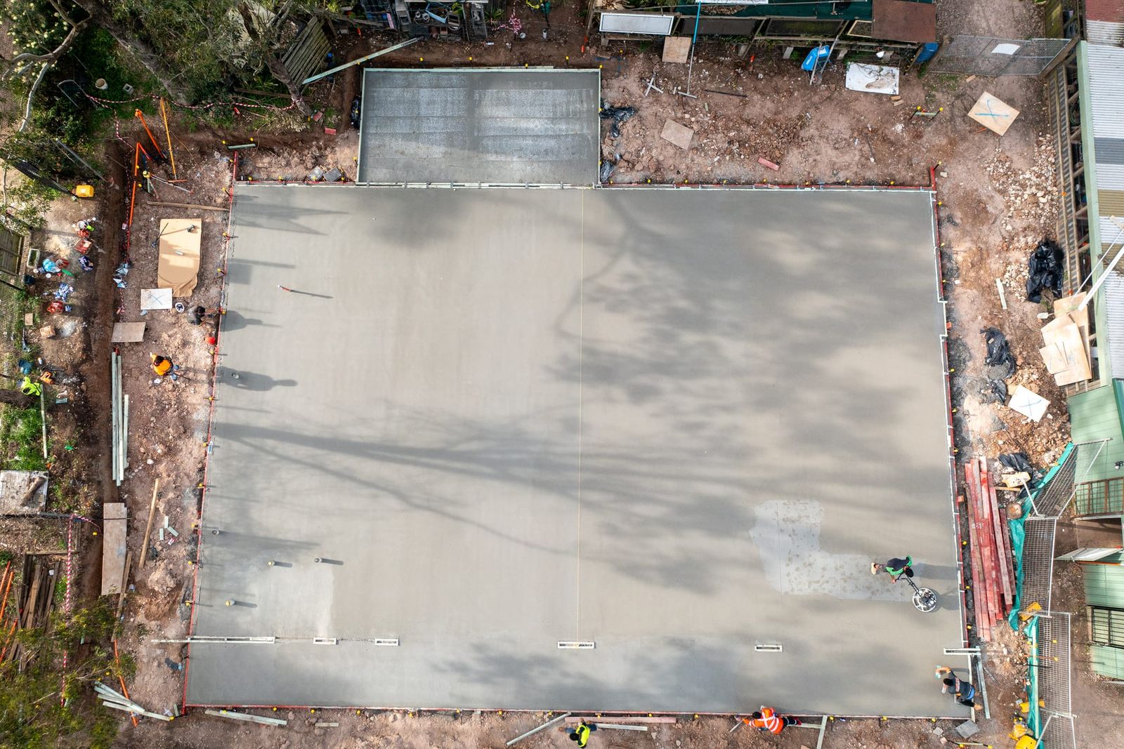 Top-down view of the finished slab inside its edge formwork, tree shadows across the concrete