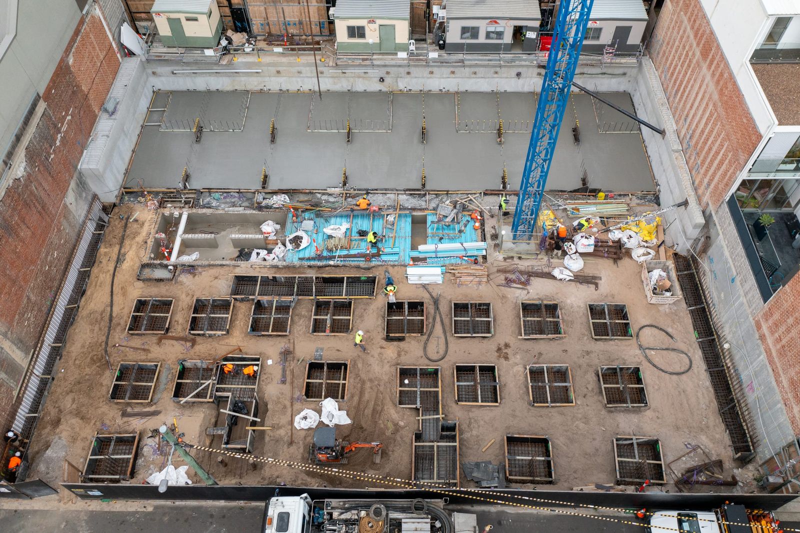 Looking straight down into the basement, square footing pits with reinforcement and crew across the floor