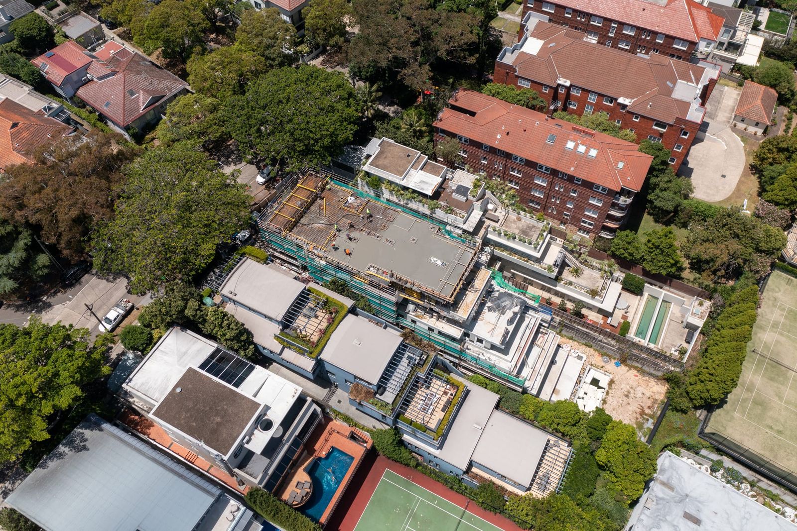 Top-down view of the site stepping down its block between houses, tennis courts and a swimming pool