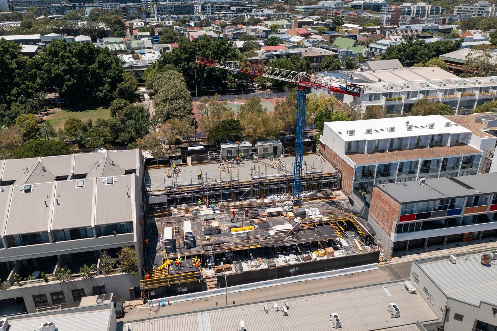 Formwork deck with yellow edge protection between townhouses, the tower crane above and the suburb beyond