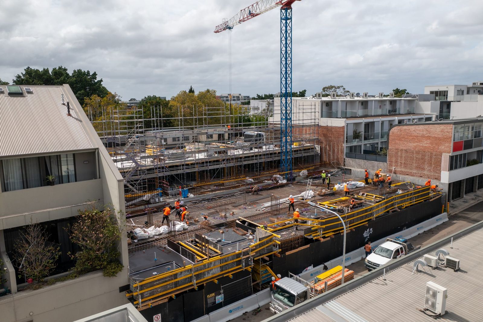 Low view across the formwork deck, crew working behind yellow edge protection under an overcast sky