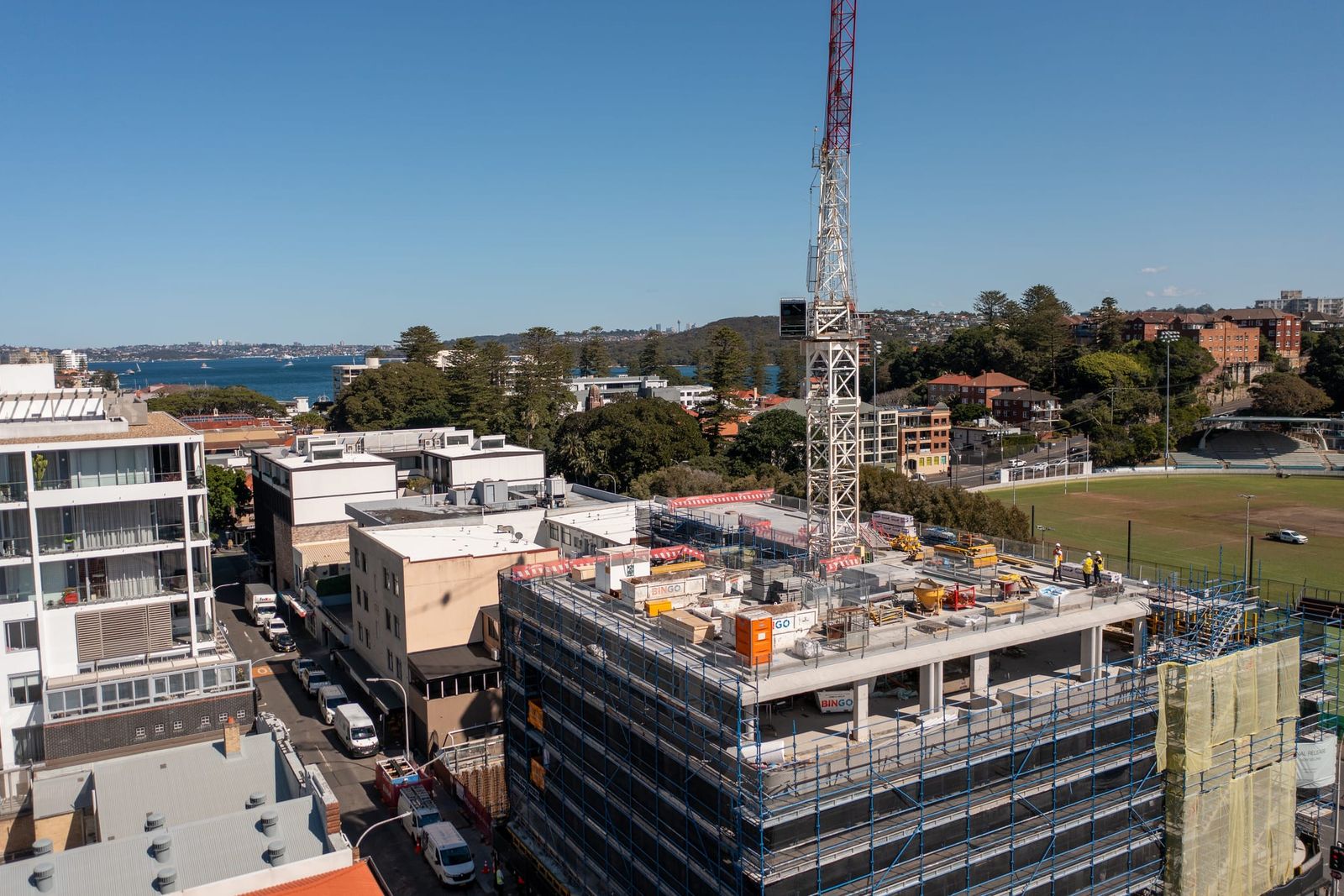 Close view of the scaffolded top floor and the tower crane mast, the harbour and oval in the background
