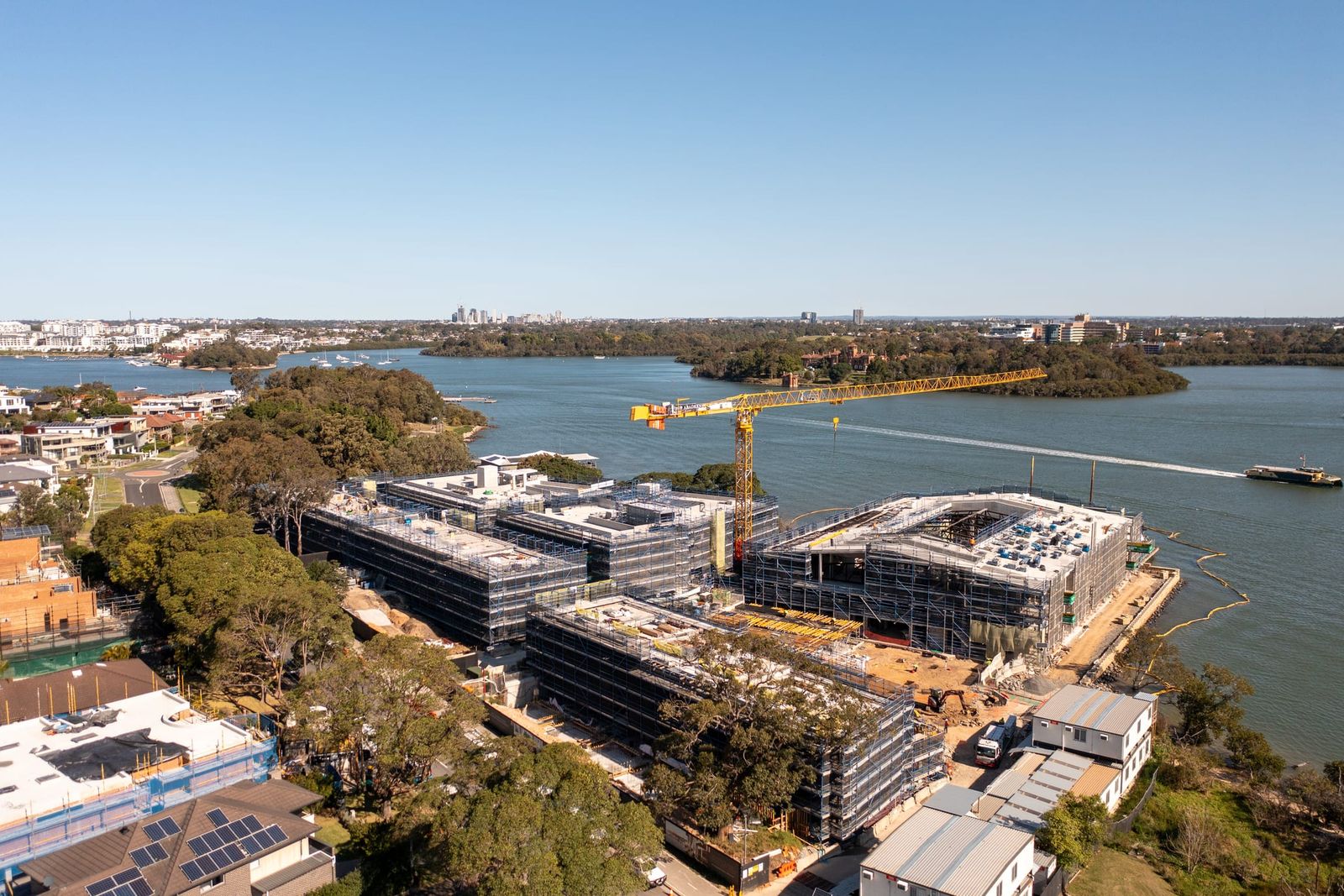 Wide view up the river, the scaffolded buildings on the foreshore beside bushland and a boat wake on the water