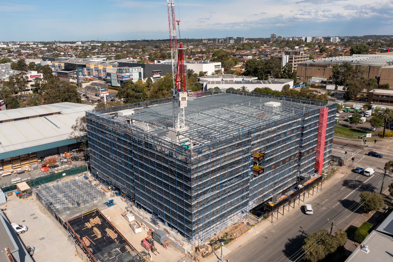 Corner view of the building wrapped in scaffold, a tower crane on the roof and a hoist on one face