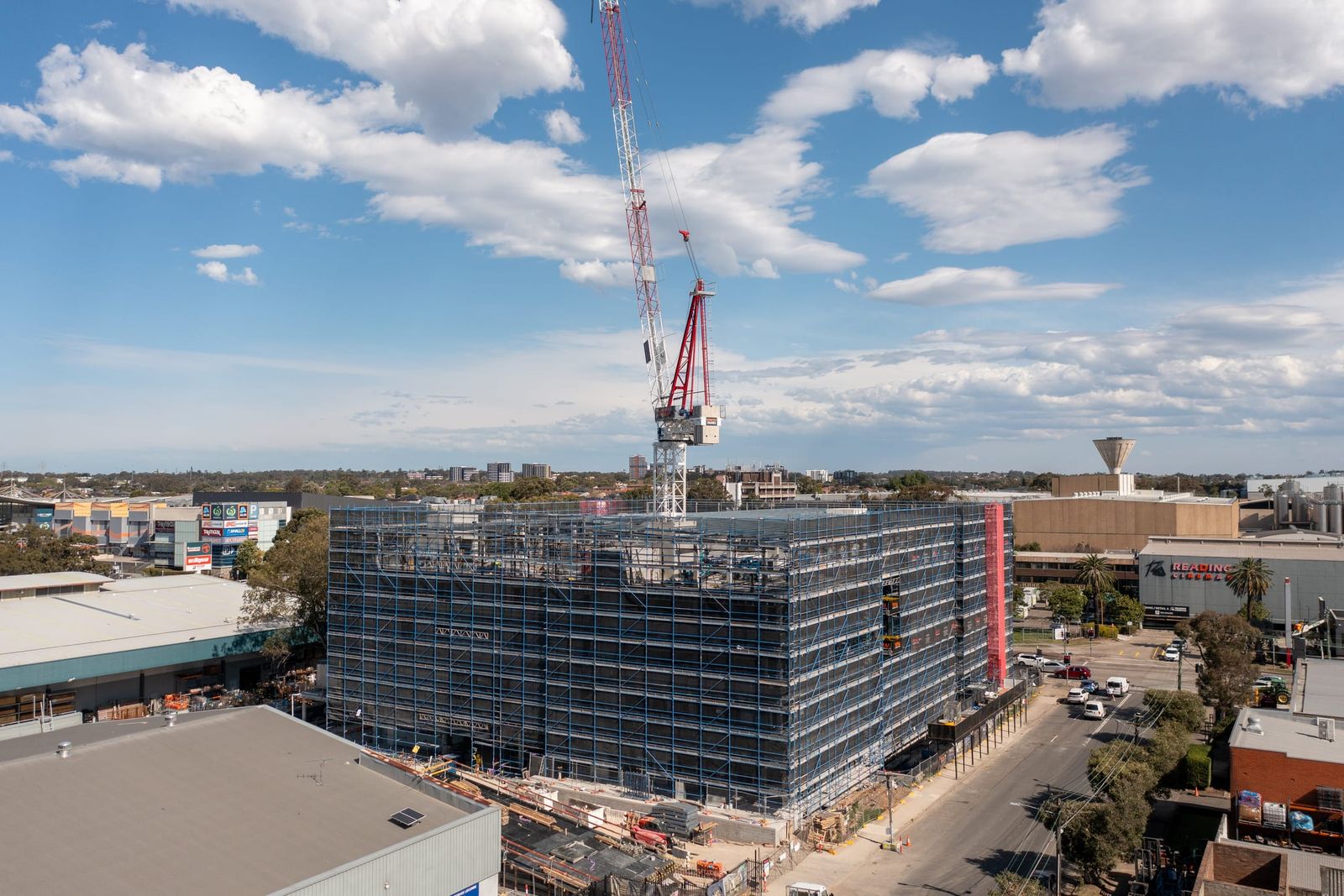 Front view of the scaffolded building and tower crane under a blue sky with scattered cloud
