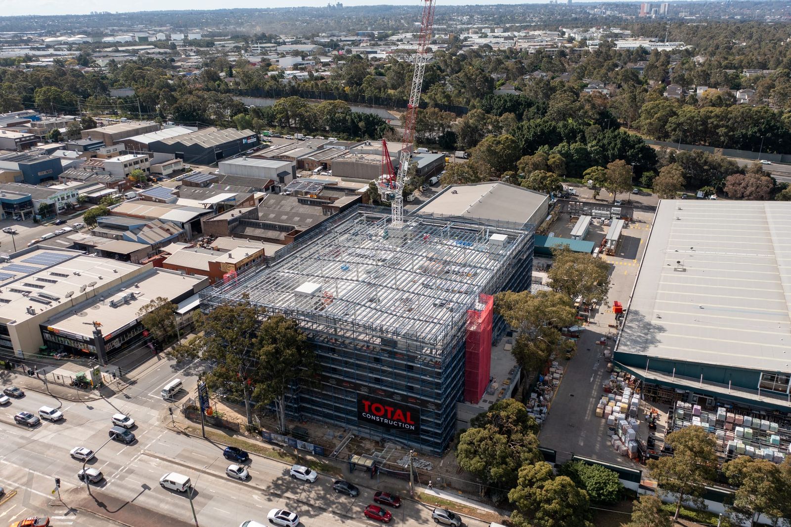 The building from across the road, scaffold wrap and a red banner on the facade, warehouses behind