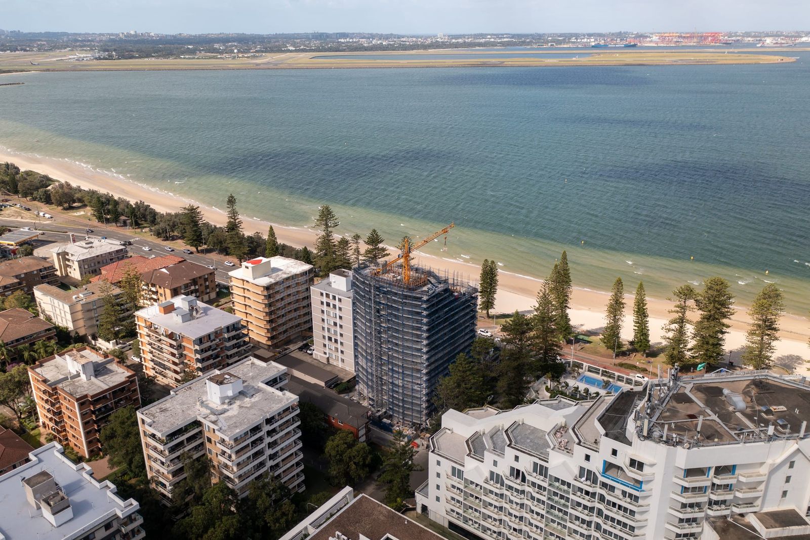 Wide view across Botany Bay to the airport runways, the scaffolded tower among the beachfront apartments