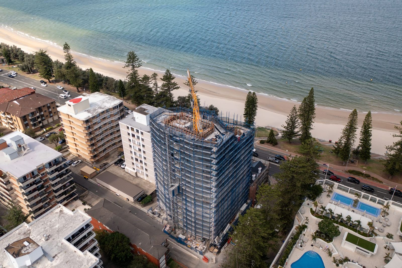 Close aerial of the scaffold wrap and the crane on the roof, the beach and pines behind