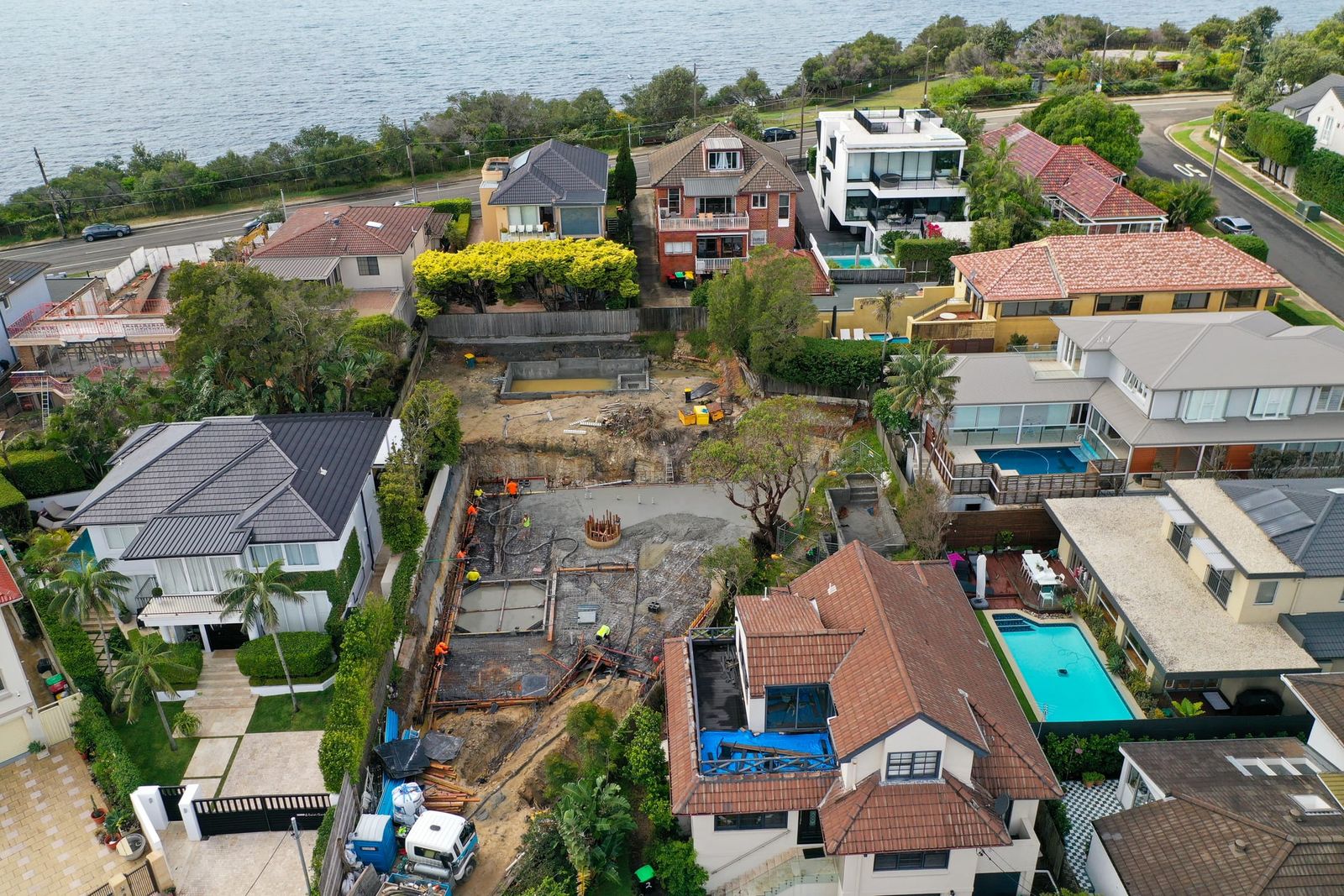 Angled view over the excavation between two homes, reinforcement and the first concrete in the base, the ocean road beyond
