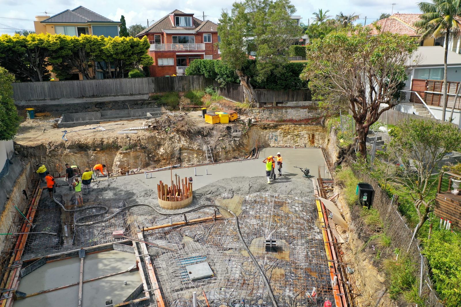 Crew placing concrete over reinforcement in the excavation, cut rock walls and a column cage in the slab