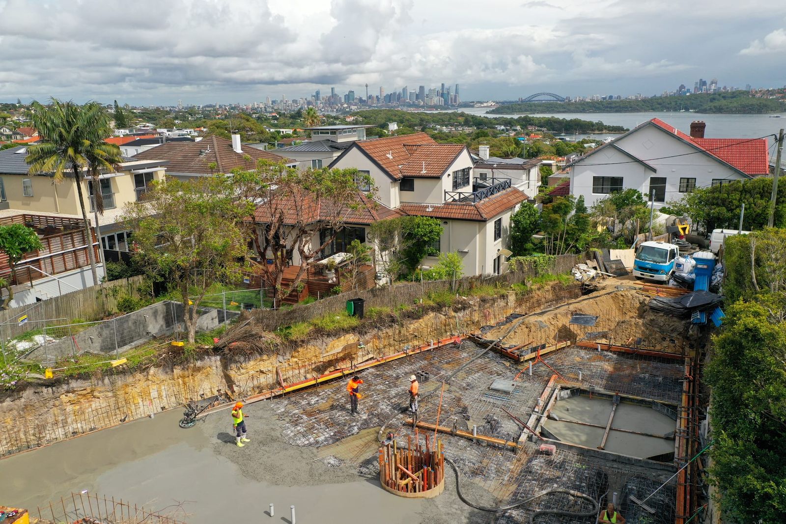Crew working the basement pour, the harbour, the Harbour Bridge and the city skyline across the water