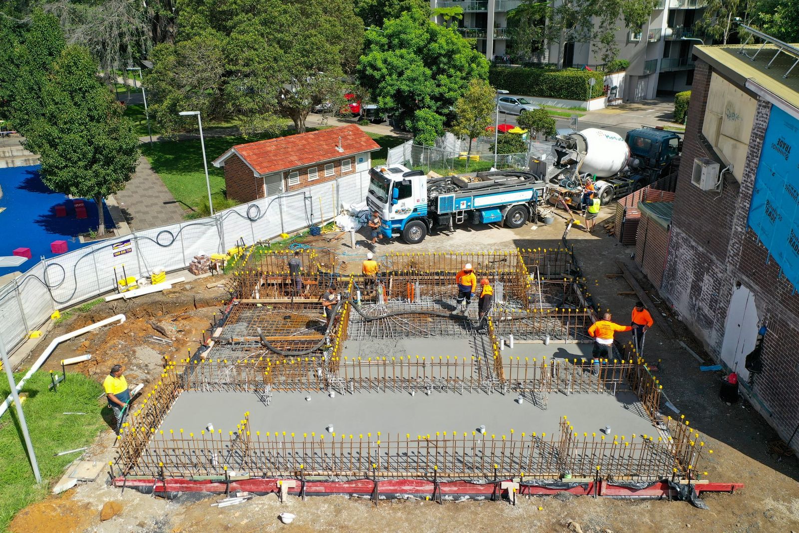 Crew placing concrete over the reinforcement, the pump truck and agitator parked at the edge of the site