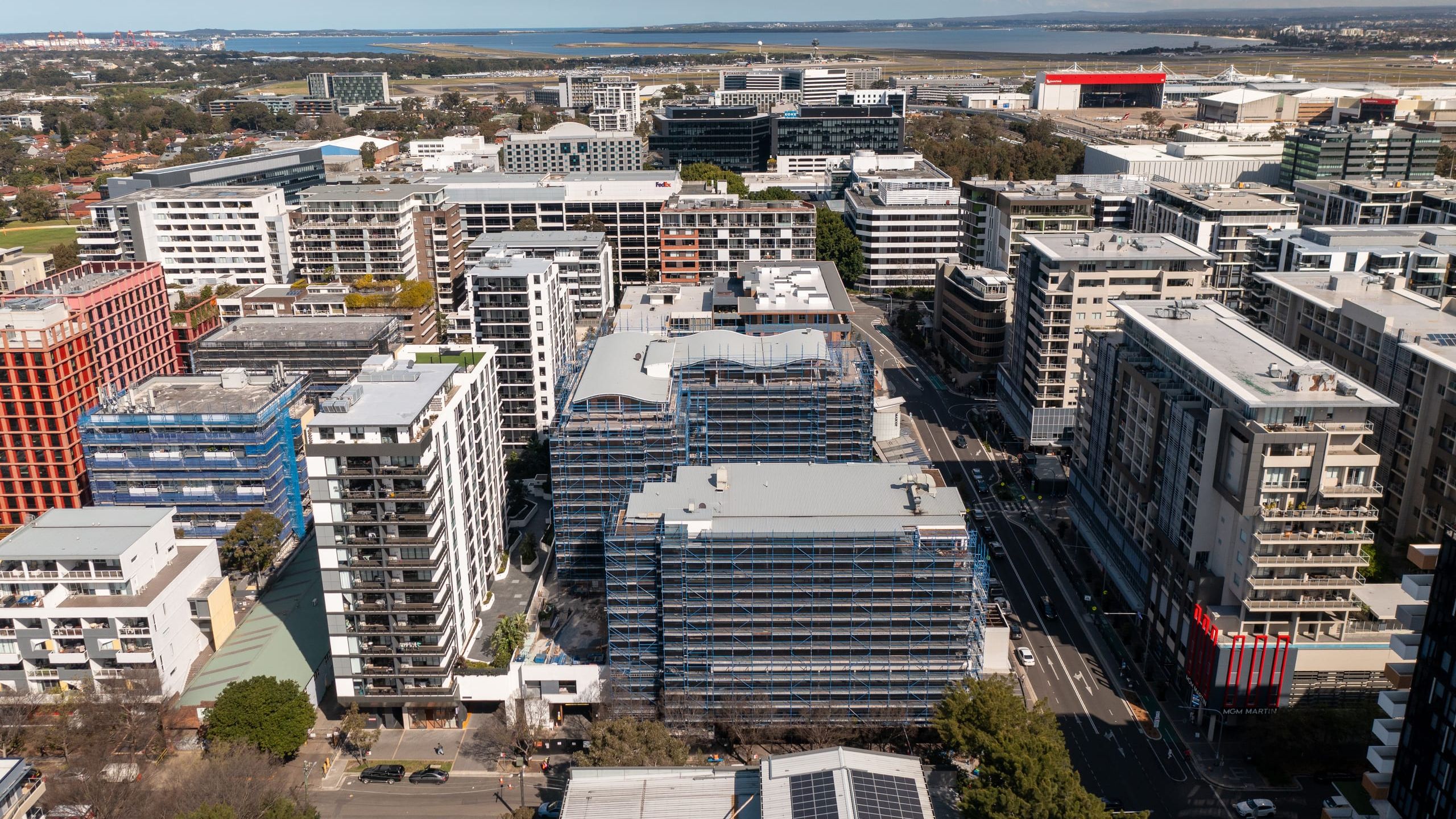 Aerial view over Mascot's apartment precinct, the scaffolded buildings among towers with the airport and Botany Bay on the horizon