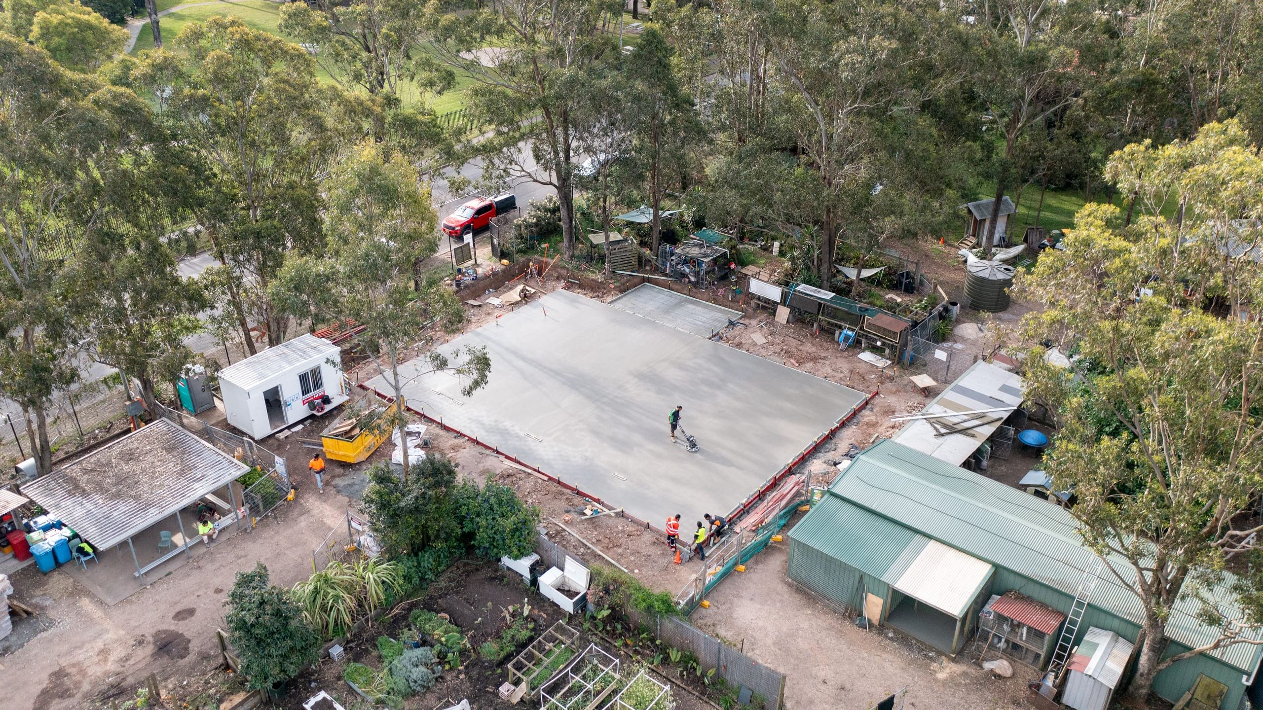 Aerial view of a freshly poured ground slab in Colyton, a worker finishing the surface among gum trees, sheds and a site office