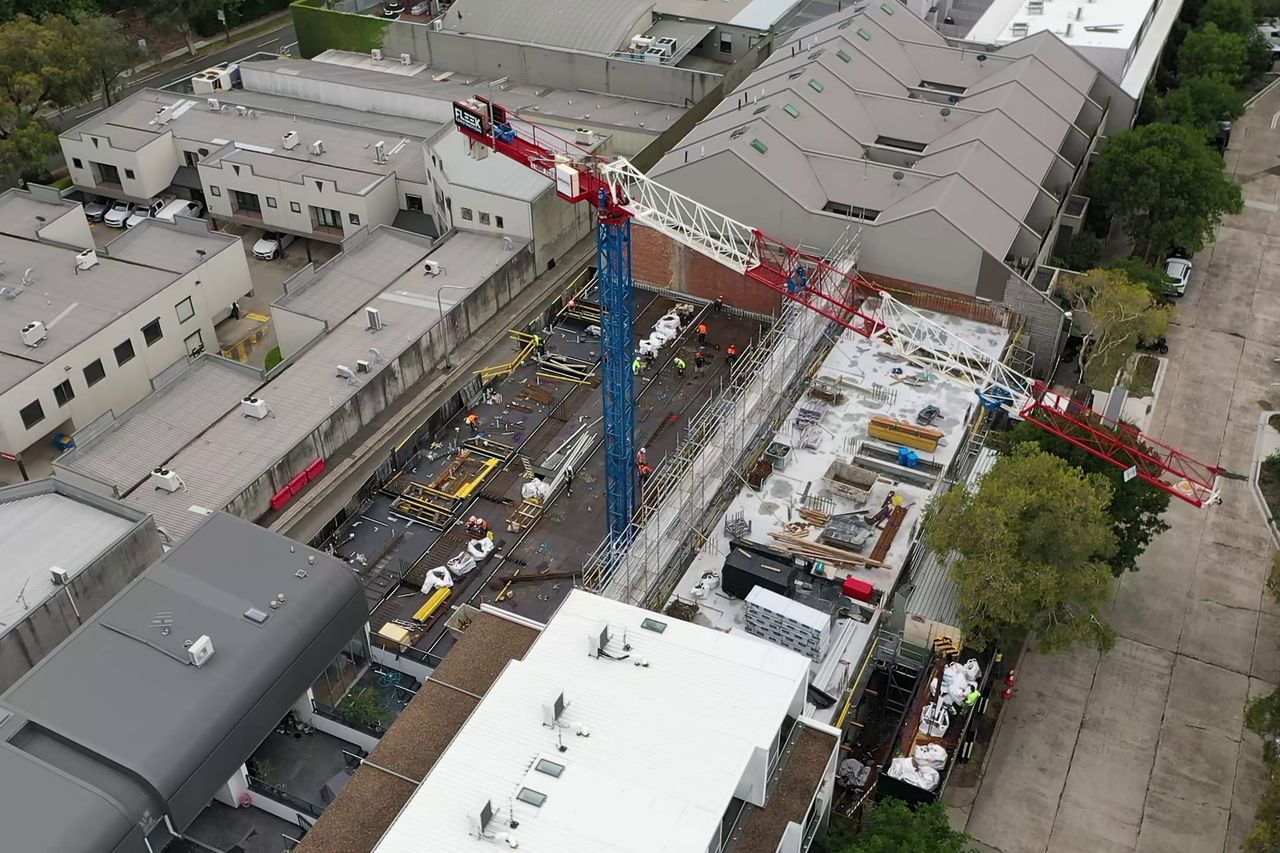 Aerial view of the Alexandria site, a blue and red tower crane over the formwork deck between industrial buildings
