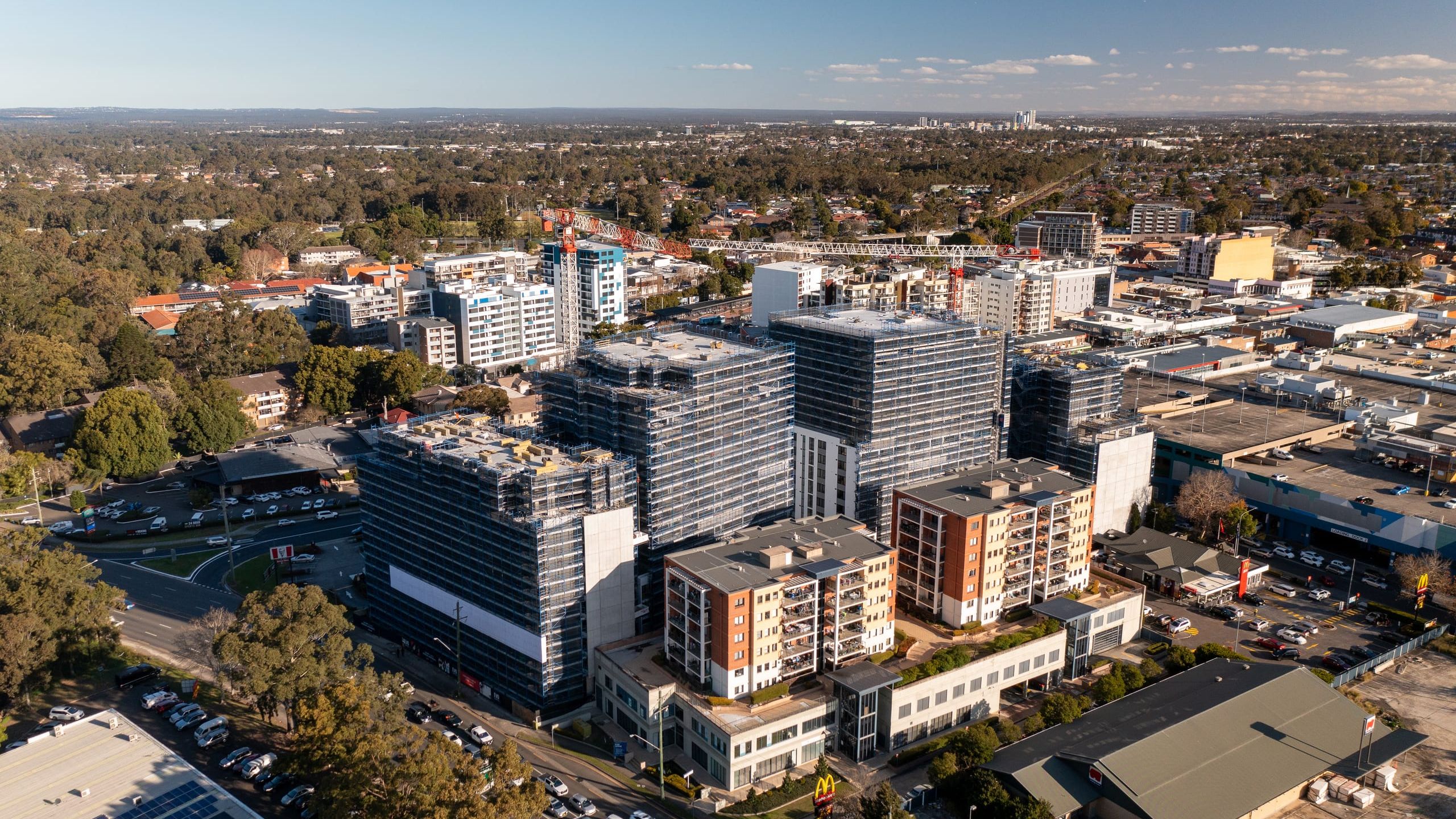 Aerial view of the Fairfield town centre in late sun, scaffolded residential towers rising beside lower apartment blocks and shops