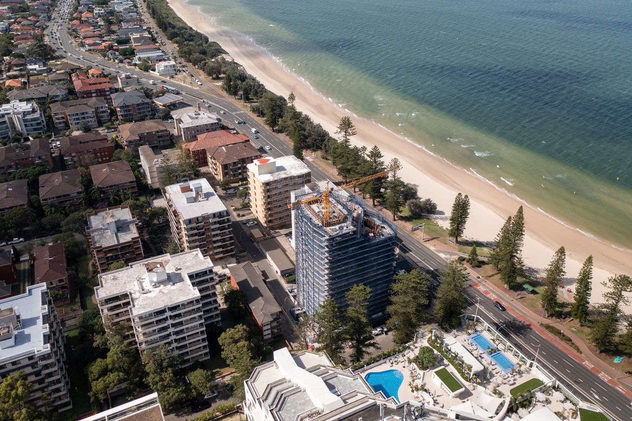 Aerial view along the Brighton Le Sands foreshore, the scaffolded tower beside the beachfront road with Botany Bay alongside