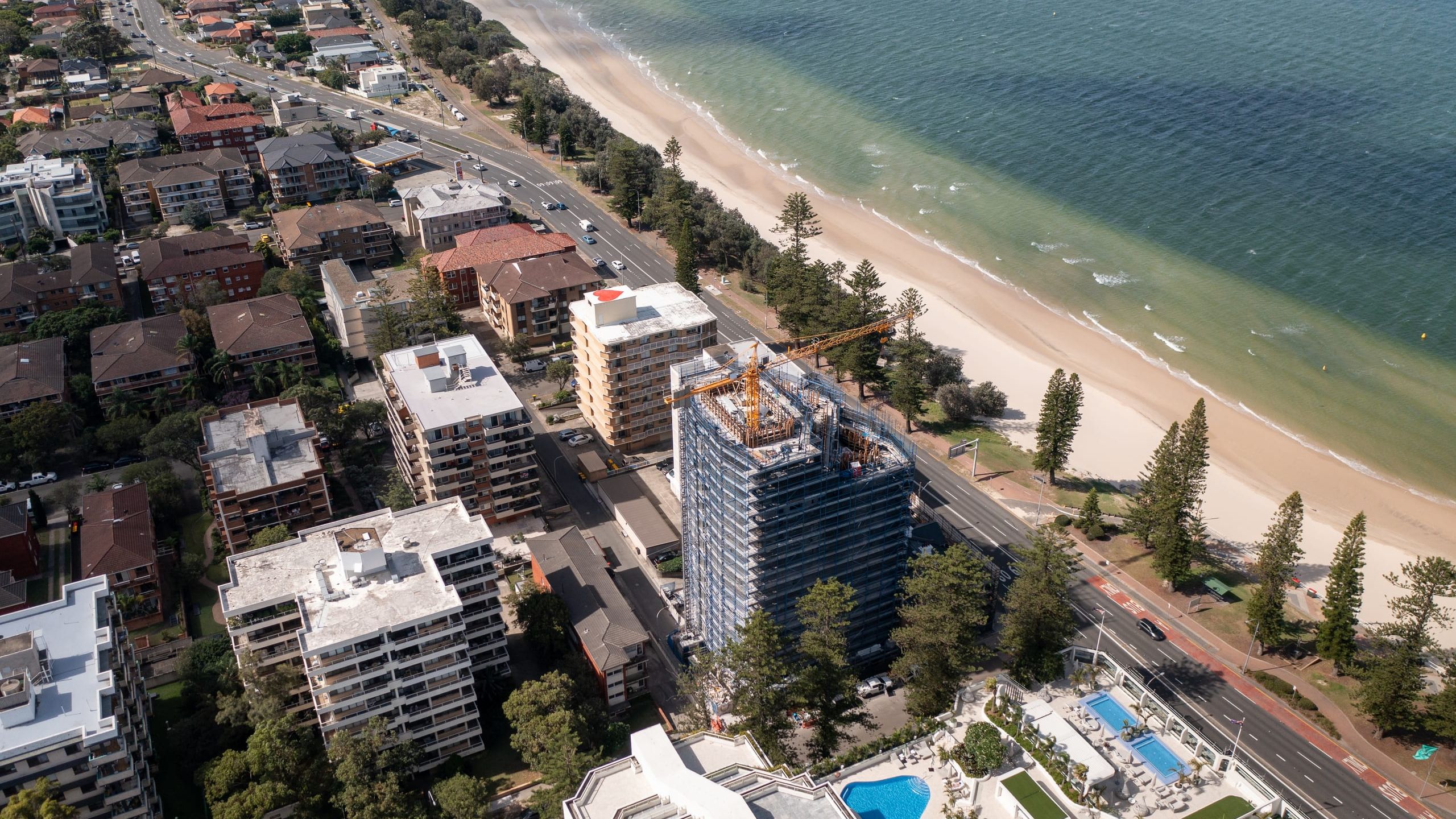 Aerial view along the Brighton Le Sands foreshore, the scaffolded tower beside the beachfront road with Botany Bay alongside