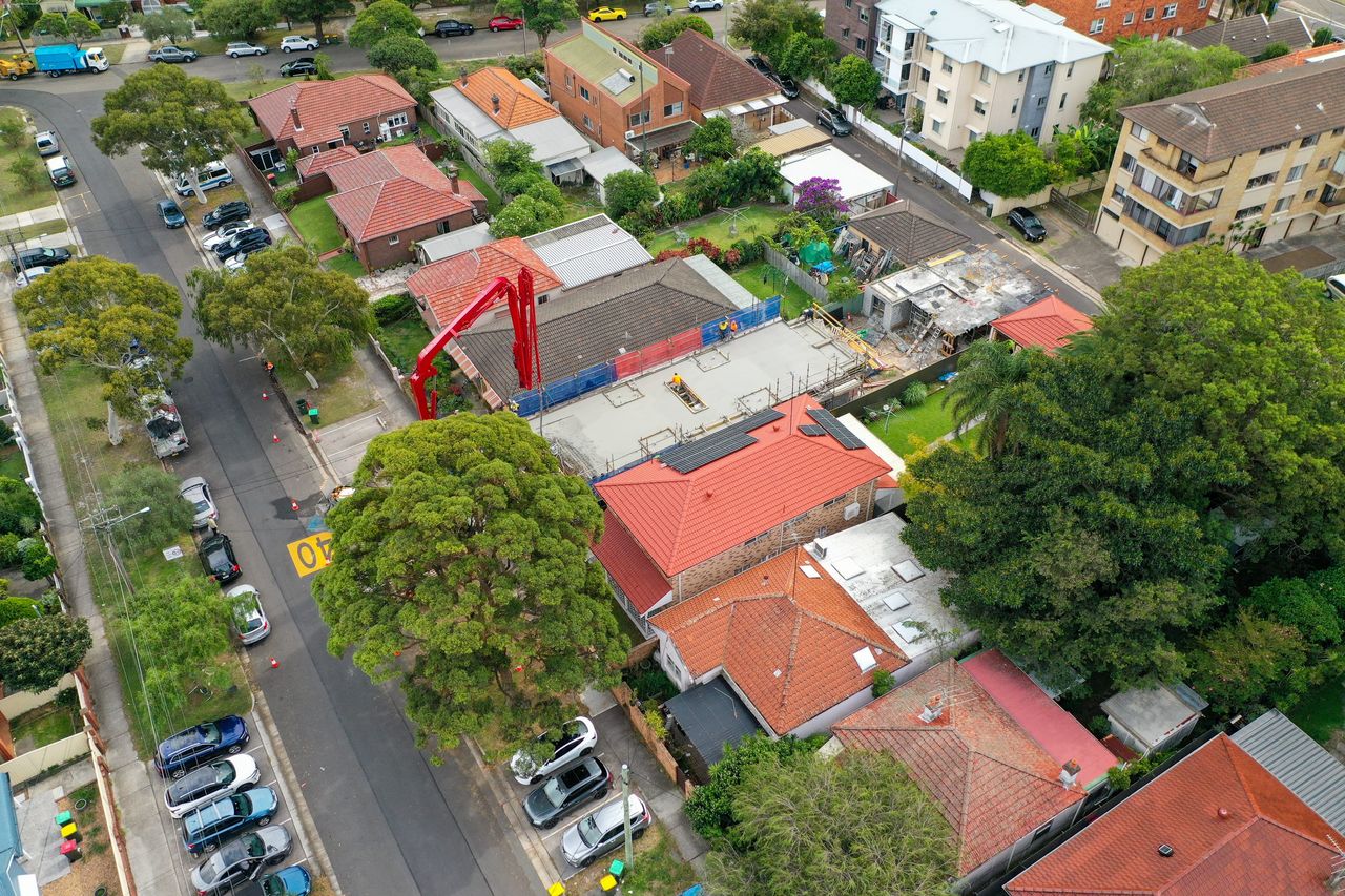 Kingsford from above, the site between houses on a tree-lined street, a red boom pump reaching over the neighbouring roof