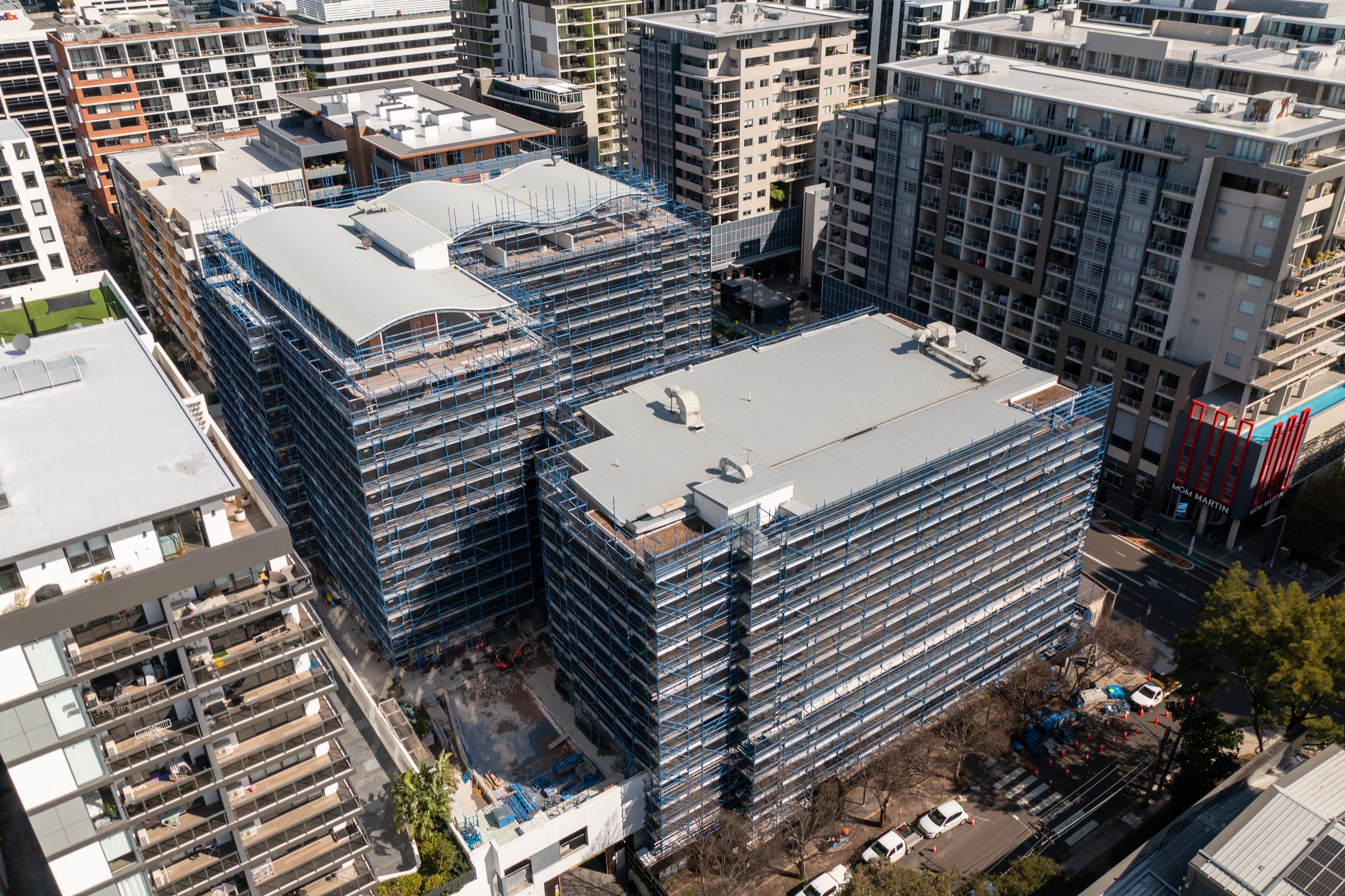 Close aerial of the two apartment buildings wrapped in blue scaffold from ground to roof