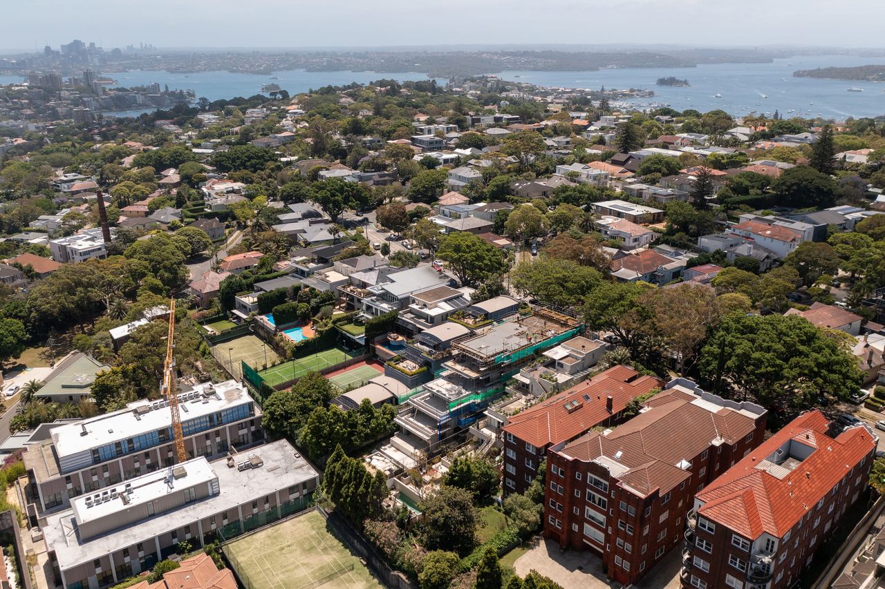 Bellevue Hill from above, the green-wrapped build among red-brick apartment blocks with Sydney Harbour and the city skyline behind